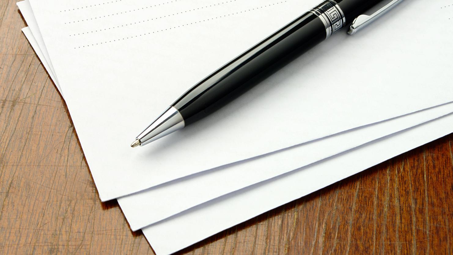 Schwarzer Kugelschreiber liegt auf einem Stapel weißer Blätter auf einer Holzoberfläche.