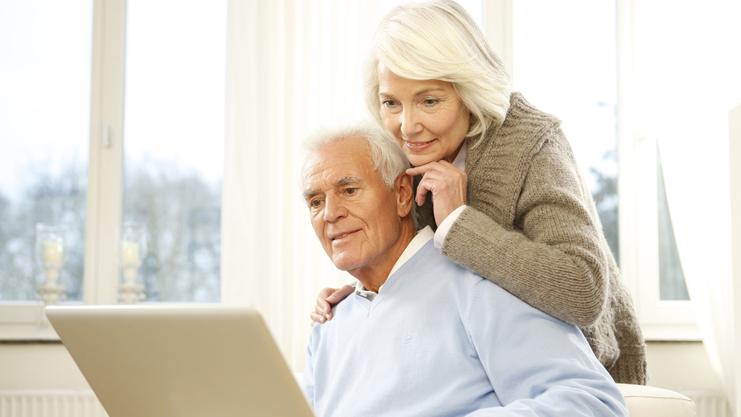 Paar sitzt auf einer Couch und schaut gemeinsam auf einen Laptop in einem hellen Raum.